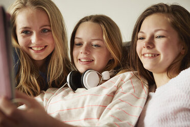 Three girls on sofa using digital tablet - CUF27564