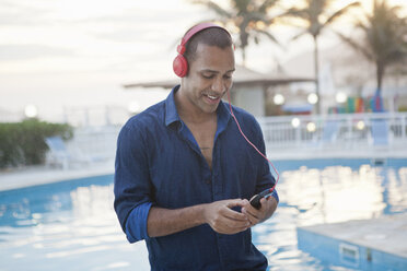 Mittlerer Erwachsener, der am Hotelpool mit seinem Smartphone Musik auswählt, Rio De Janeiro, Brasilien - CUF27567