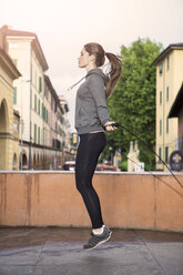 Side view of woman wearing sports clothes using skipping rope - CUF27622