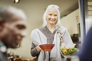 Ältere Frau trägt Schüsseln mit Salat nach draußen - CUF27646