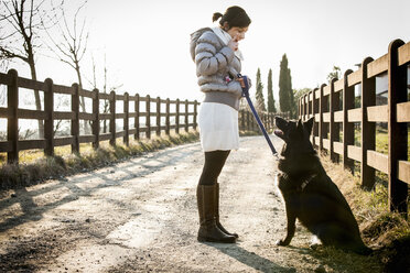 Mittlere erwachsene Frau, die ihren Hund auf der Landstraße zum Sitzen bringt - CUF27691