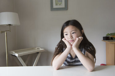 Fed up girl at table with chin in hands - CUF27705