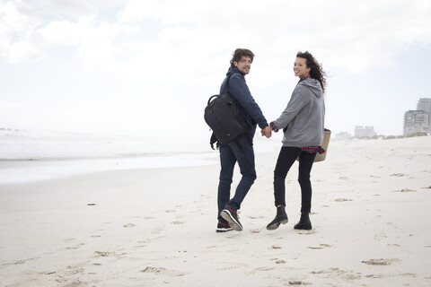 Rückansicht eines jungen Paares, das am Strand spazieren geht, Westkap, Südafrika, lizenzfreies Stockfoto