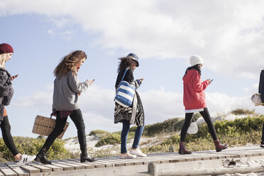 Reihe junger Erwachsener, die an der Strandpromenade entlang schlendern und Smartphones lesen, Westkap, Südafrika - CUF27729