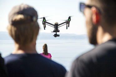 Rear view of man and woman looking at drone flying mid air over coast, Split, Dalmatia, Croatia - CUF27753