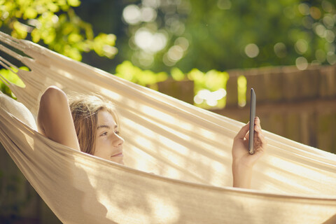 Jugendlicher, der in einer Hängematte im Garten liegt und auf einem digitalen Tablet surft, lizenzfreies Stockfoto