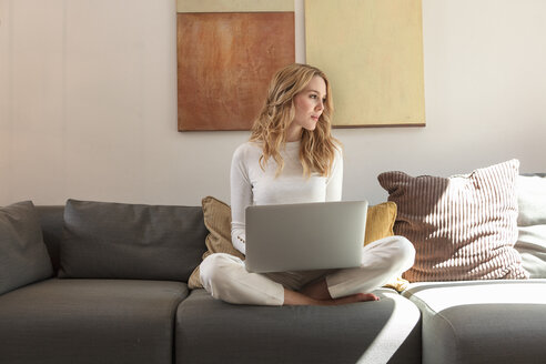 Frau auf Sofa mit Laptop und Blick in die Ferne - CUF27834