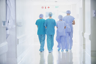 Rear view of four medical staff wearing scrubs walking in hospital corridor - CUF27909