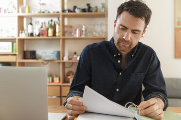 Man with laptop looking at paperwork - CUF27936