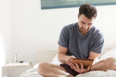 Mann sitzt auf dem Bett und benutzt ein digitales Tablet - CUF27942