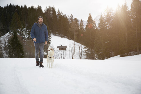 Mann geht mit Hund in verschneiter Landschaft spazieren, Elmau, Bayern, Deutschland - CUF27957
