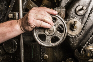 Close up of mans hand operating printing machinery in printing press workshop - CUF27960