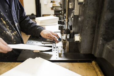 Male printer preparing paper for printing machinery in printing press workshop - CUF27962