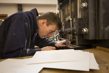 Young male printer preparing printing machinery in printing press workshop - CUF27963