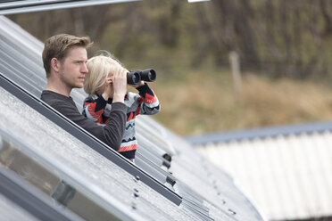 Father and son looking through rooflight, boy using binoculars - CUF28022