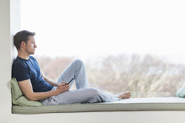 Mid adult man sitting on window seat, looking out of window - CUF28051