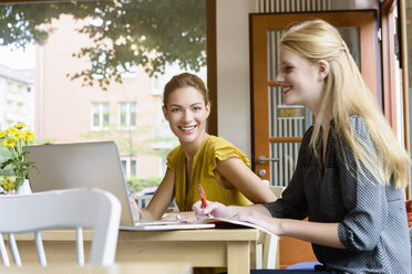 Two young women using laptop and writing notes in cafe - CUF28053