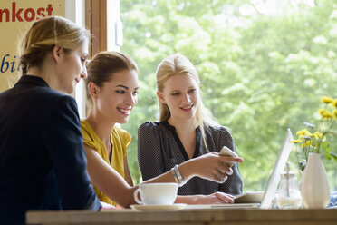 Drei junge Frauen, die auf einen Laptop in einem Café zeigen - CUF28056