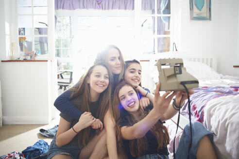 Vier Teenager-Mädchen machen ein Selfie mit Sofortbildkamera im Schlafzimmer - CUF28110