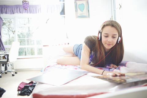 Teenager-Mädchen, das eine Schallplattenhülle betrachtet, während es im Schlafzimmer Kopfhörer hört, lizenzfreies Stockfoto