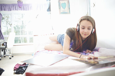 Teenager-Mädchen, das eine Schallplattenhülle betrachtet, während es im Schlafzimmer Kopfhörer hört - CUF28117