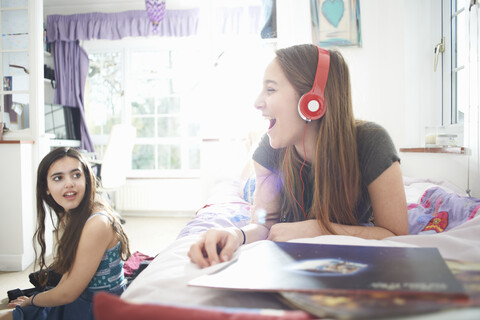 Teenager-Mädchen, das sich mit einem Freund unterhält, während es im Schlafzimmer Kopfhörer hört, lizenzfreies Stockfoto