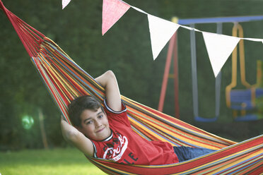 Portrait of confident boy reclining in striped garden hammock with hands behind head - CUF28158