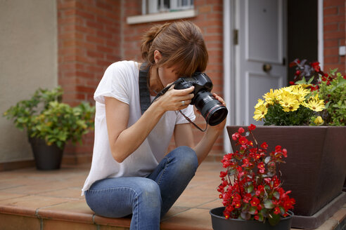 Mittlere erwachsene Frau, die im Freien sitzt und einen Blumentopf fotografiert - CUF28206