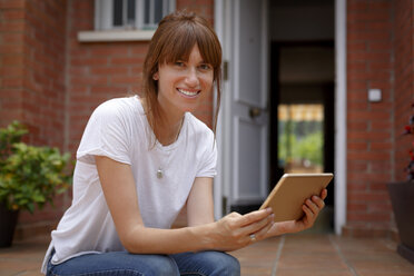 Mittlere erwachsene Frau sitzt im Freien, hält ein digitales Tablet und schaut in die Kamera - CUF28207