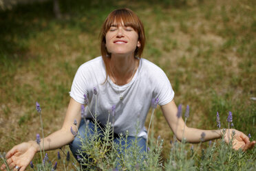 Mid adult woman crouching smelling lavender, eyes closed, arms open - CUF28225