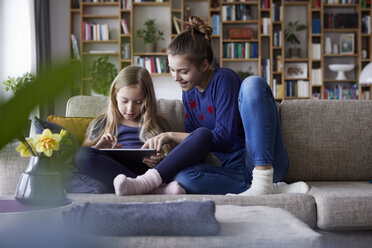 Zwei Schwestern sitzen auf dem Sofa und spielen mit einem digitalen Tablet - RBF06239