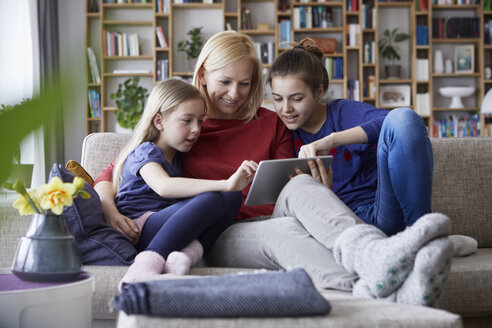 Mother and her daughters sitting on couch, having fun using digital laptop - RBF06241