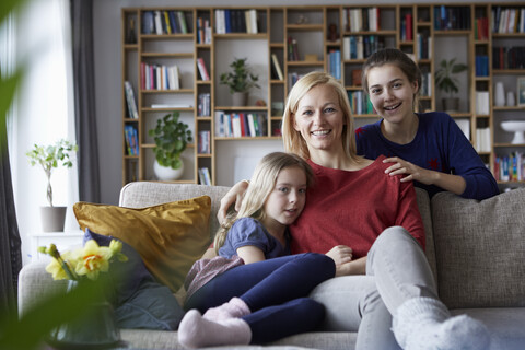 Mother and her daughters cuddling and having fun, sitting on couch stock photo