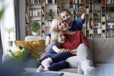 Mutter und ihre Töchter sitzen auf der Couch und machen Smartphone-Selfies - RBF06251