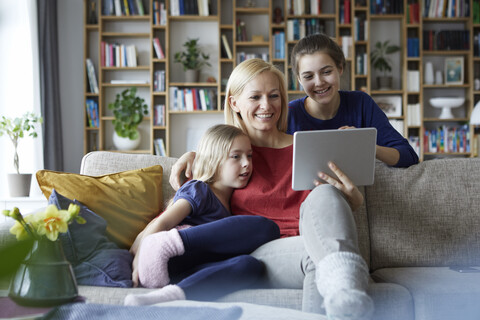 Mother and her daughters sitting on couch, having fun using digital laptop stock photo