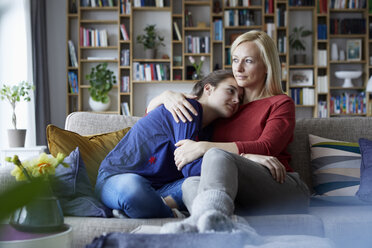 Mutter und heranwachsende Tochter sitzen auf der Couch und halten sich in den Armen - RBF06255