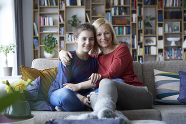 Mutter und heranwachsende Tochter sitzen auf der Couch und halten sich in den Armen - RBF06256