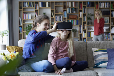 Sisters sitting on couch, playing with VR glasses - RBF06257