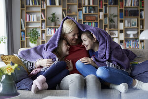 Mutter und ihre Töchter kuscheln und haben Spaß, sitzen auf der Couch, in eine Decke gehüllt - RBF06259