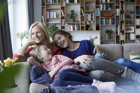 Mother and her daughters cuddling and having fun, sitting on couch - RBF06260