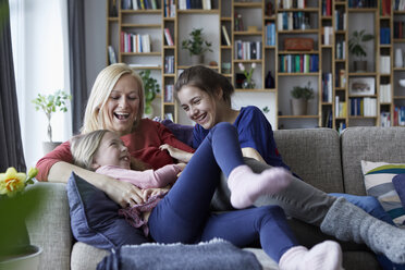 Mother and her daughters cuddling and having fun, sitting on couch - RBF06261