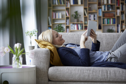 Frau mit digitalem Tablet, entspannt auf der Couch, lizenzfreies Stockfoto