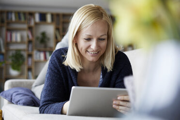 Woman using digital tablet, relaxing on couch - RBF06270