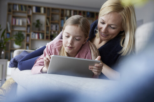 Mutter und Tochter liegen auf der Couch und benutzen ein digitales Tablet - RBF06273