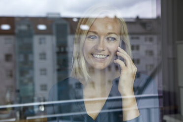 Blond woman standing at window, talking on the phone - RBF06278