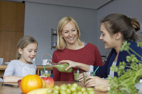 Mother with daughters sitting in kitchen, drinking homemade fruit smoothie - RBF06279