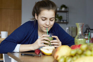 Girl sitting in kitchen, drinking homemade fruit smoothie - RBF06281