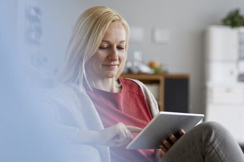 Blond woman sitting at home, using digital tablet stock photo