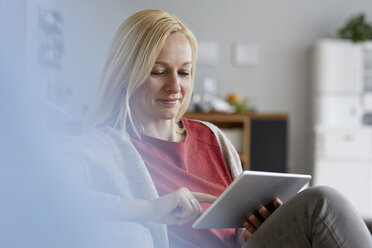 Blonde Frau sitzt zu Hause und benutzt ein digitales Tablet - RBF06292