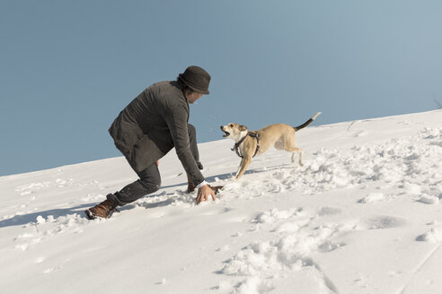 Man playing with dog in winter, throwing snow - REAF00277